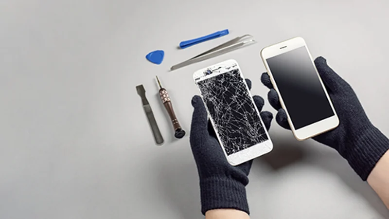 Handen met werkhandschoenen houden een telefoon met gebarsten scherm vast, naast reparatiegereedschap.